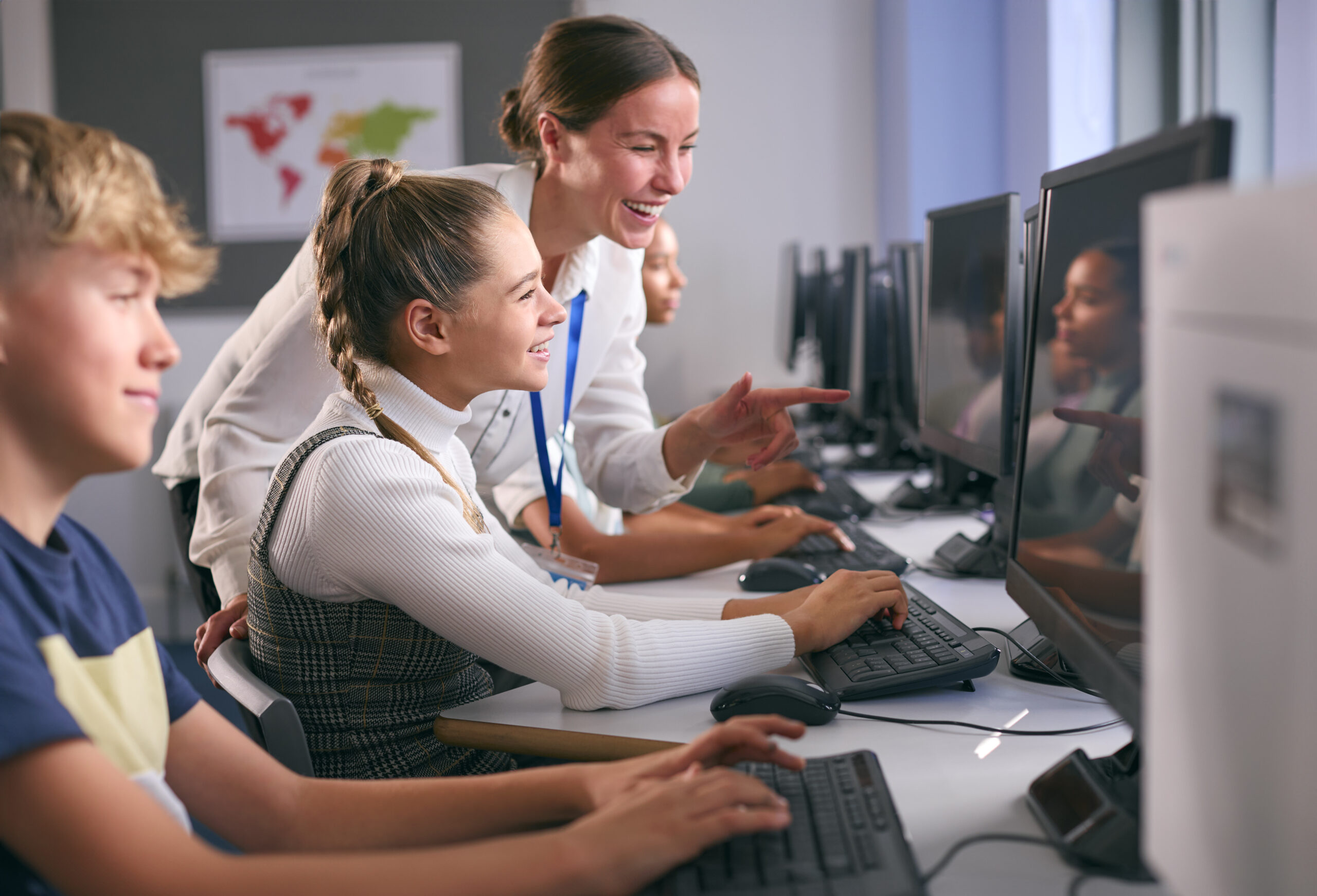 Group Of Secondary Or High School Students At Computers In IT Class With Female Teacher demonstrating the concept of adaptive learning