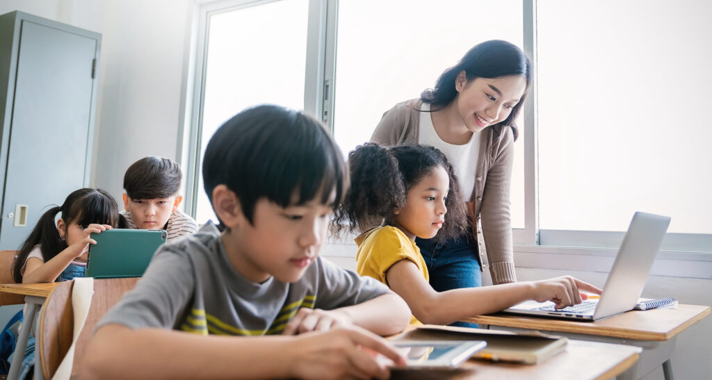 Un niño, una niña y un profesor utilizando un ordenador en el aula de primaria. Mostrando el concepto de superación de retos de evaluación.