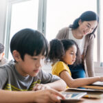 Jeune garçon, jeune fille et enseignant utilisant des ordinateurs dans une salle de classe d'école primaire. Montrant le concept de surmonter les défis de l'évaluation.