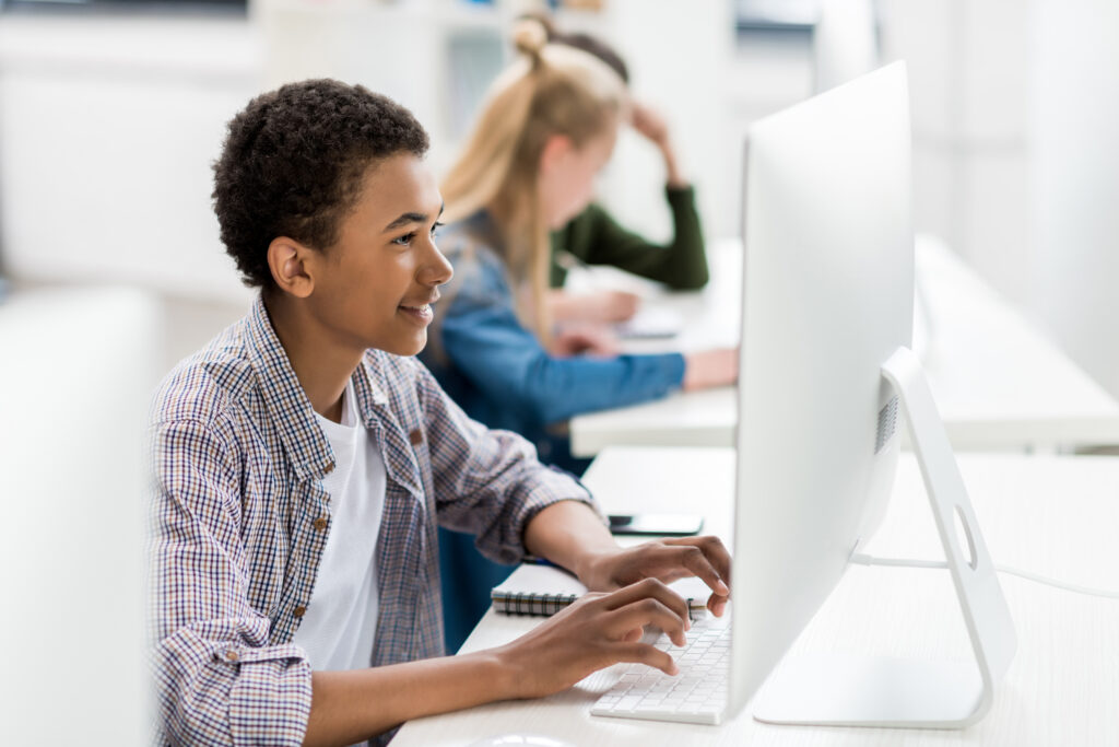 side view of african american teen boy typing on keyboard in front of computer screen in class