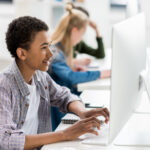 side view of african american teen boy typing on keyboard in front of computer screen in class