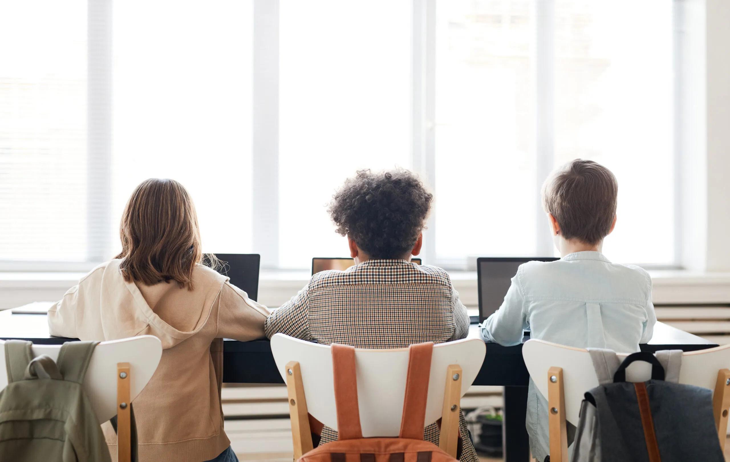 View from behind of three children sitting in a row in front of their computers.